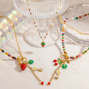Detailed shot of gold necklaces with pearls, strawberries, and daisies on glassware