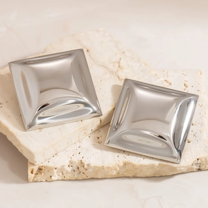Macro shot of minimalist silver square stud earrings on natural travertine stone background