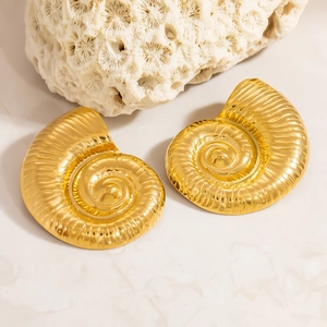 Detailed macro view of gold spiral seashell earrings on a white coral stone background