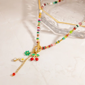Detail view of colorful bead necklace with cherry and daisy charms on a marble surface