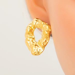Close-up of golden irregular earrings with hammered metal texture on model ear