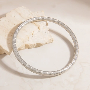 Macro detail of silver stainless steel twisted bangle on a minimalist stone display