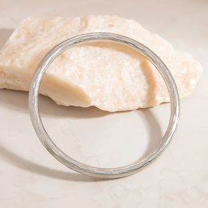 Detailed close-up of textured silver stainless steel bangle against a marble background