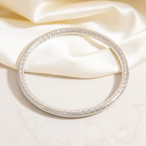 Close-up of silver stainless steel bangle with intricate woven texture and metallic luster