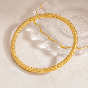 Detail of 18K gold stainless steel bracelet with intricate spiral engraved texture on marble