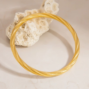 Macro view of 18K gold-plated twisted mobius bangle with frosted texture on white coral