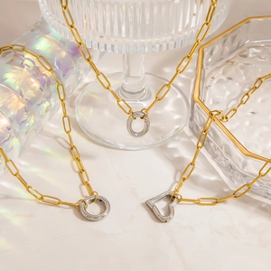 Detail of silver heart and circle pendants on a golden paperclip chain with elegant shadows