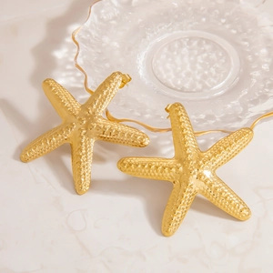 Close-up of golden starfish earrings with textured surface on marble background
