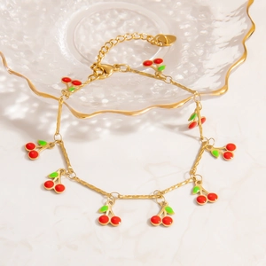 Elegant gold cherry necklace and bracelet set with red enamel charms on marble background