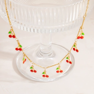 Golden stainless steel necklace featuring red cherry pendants hanging on a glass tray