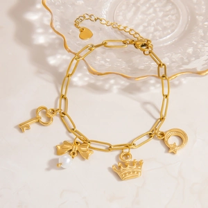 Detailed view of 18K gold plated bracelet with pearl bow and heart charms on stone surface