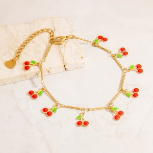 Detail of gold cherry charm anklet with red enamel fruits on marble background