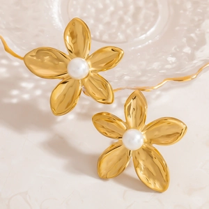 Elegant gold flower stud earrings with central pearl on a decorative glass tray