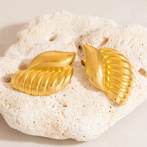 Detailed view of gold leaf stud earrings with realistic textures on a white coral stone