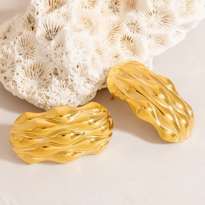 Detailed macro of gold plated ocean wave earrings placed on white coral and sand