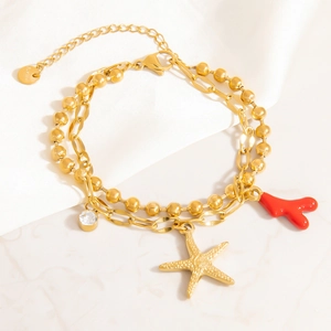 Dettaglio di un bracciale in acciaio inossidabile dorato con ciondoli a stella e corallo