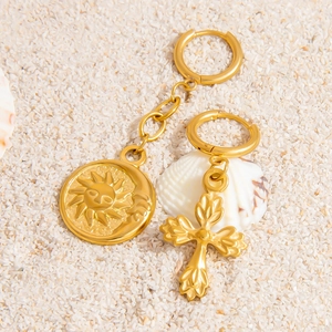 Dettaglio di ciondoli a croce sole e luna placcati in oro 18K su sabbia bianca fine