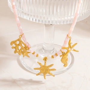Pink stone beaded necklace with golden sun, seahorse and starfish pendants on marble