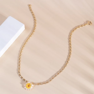 Close-up of golden necklace with a white and yellow daisy flower pendant on beige background