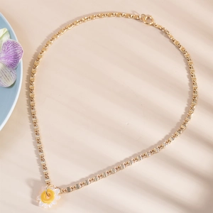 Minimalist gold necklace with a white daisy pendant featuring natural light and shadows