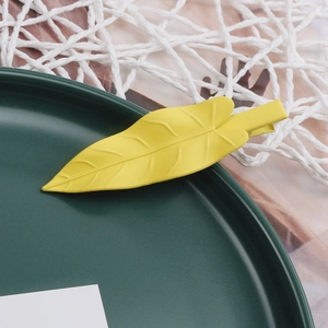 Detail of yellow leaf-shaped hair clip with matte finish and duckbill clamp design