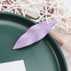 Close-up of a matte purple leaf-shaped hair clip on a dark green textured plate