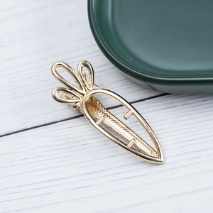 Hollow carrot shaped golden alloy hair clip with non-slip texture on wood background