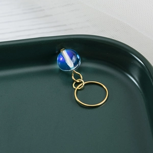 Macro shot of minimalist gold ring with a cosmic blue glass sphere charm on dark tray