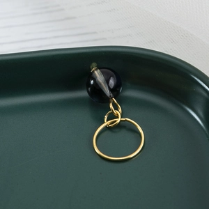 Golden dreadlock ring with a deep blue translucent bead on dark green tray