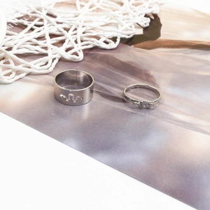 Detail of silver couple rings with wavy cutout designs on a purple textured backdrop