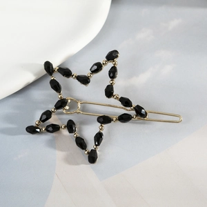 Elegant gold star hair clip with black beads on a minimalist soft blue background