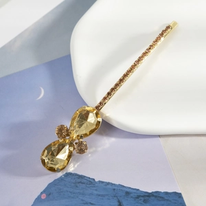 Détail macro d'une barrette dorée ornée de strass étincelants en forme de goutte champagne