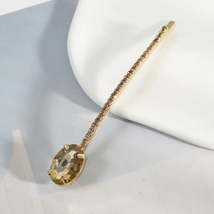 Close-up of golden hair clip with amber oval gemstone and sparkling rhinestone pavé