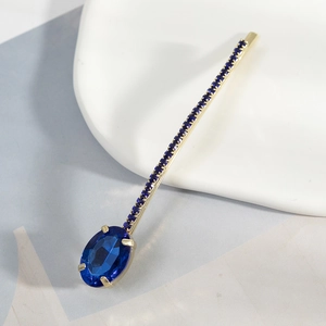 Elegant gold hair clip featuring a large oval blue gemstone and shimmering rhinestones