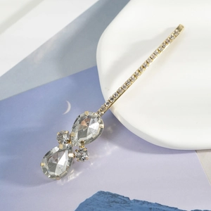 Vue détaillée de la pince à cheveux goutte d'eau dorée avec strass scintillants et noeud élégant