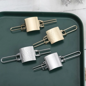 Minimalist metal arrow hair pins in gold and silver finishes on a green tray