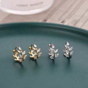 Macro detail of zircon leaf hoop earrings in gold and silver finish on a green tray