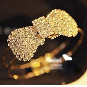 Dettaglio di un bracciale a fascia dorato a forma di fiocco con strass bianchi