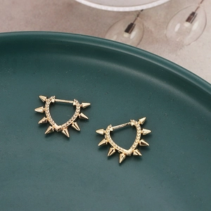 Golden heart-shaped hoop earrings with punk-style spike rivets on a ceramic plate