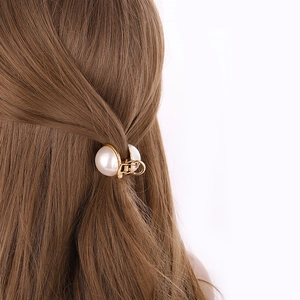 Détail d'une pince à cheveux dorée avec perles fixant une demi-queue sur cheveux bruns