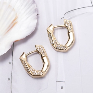 Minimalist geometric gold earrings with pavé zircon stones on a white shell background