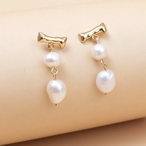 Macro detail of drop earrings featuring irregular pearls and gold metallic barbell studs