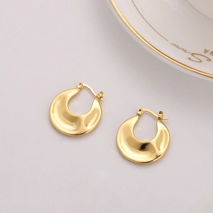 Polished gold U-shaped chunky hoop earrings with a textured surface on a beige background