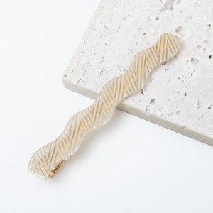 Macro detail of wave-shaped yellow resin hair clip with gold V-geometric patterns