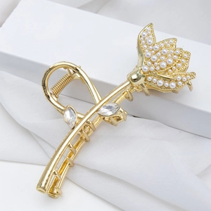Elegant gold lotus hair claw clip with pearls and rhinestones on white fabric