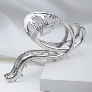 Close-up of a sleek silver irregular hollow metal hair claw clip on a stone surface