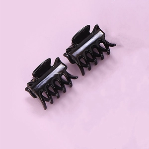 Pair of small black high-gloss plastic hair claw clips on a light purple background