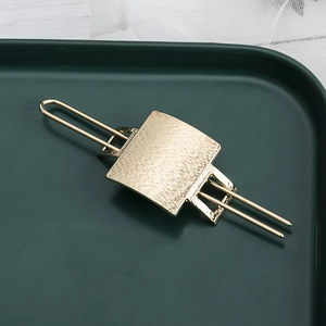 Close-up of golden brushed metal hair pin with rectangular texture detail on tray