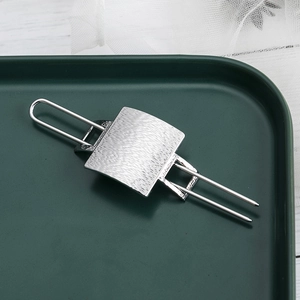 Minimalist silver brushed metal hair stick with square concave plate on green tray