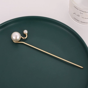 Elegant gold metal hair pin with minimalist white pearls displayed on dark green plate